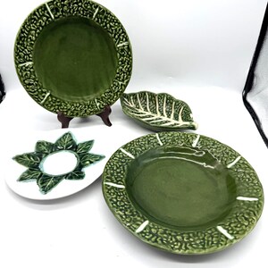 Peut inclure: Ensemble de vaisselle en céramique verte, comprenant des assiettes et un plat en forme de feuille. Les assiettes ont des bords texturés avec un motif répétitif. Une assiette est sur un petit support marron. Le plat en forme de feuille a des détails blancs.
