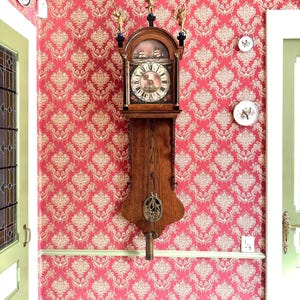 Peut inclure: Une horloge murale ancienne en bois avec un pendule est suspendue à un mur recouvert de papier peint damassé rouge. L'horloge a un cadran rond avec des chiffres romains et est ornée de petites statues. Des assiettes décoratives sont également montées sur le mur.