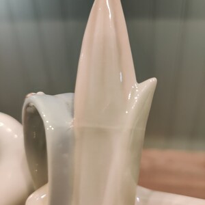 May include: A white porcelain figurine of a swan with its neck arched and head tilted back. The swan has a smooth, glossy finish and intricate details.