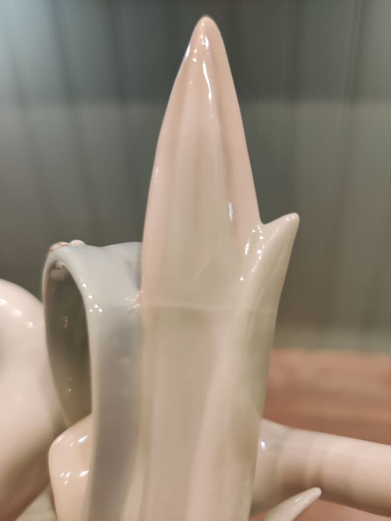 May include: A white porcelain figurine of a swan with its neck arched and head tilted back. The swan has a smooth, glossy finish and intricate details.