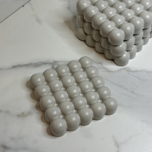 May include: Two white ceramic soap dishes with a textured bubble design. The dishes are stacked on top of each other.