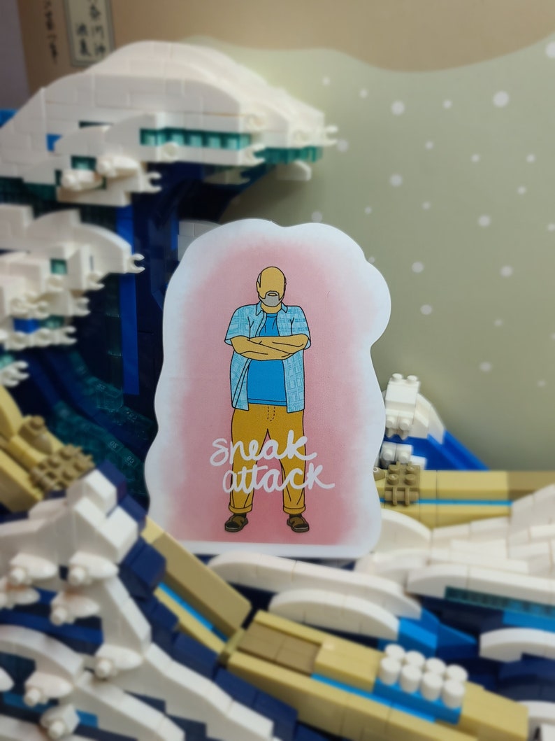 May include: A sticker featuring a cartoon man with arms crossed, wearing a blue shirt and yellow pants. The sticker has the text "sneak attack" in white script. The background is a pink cloud.