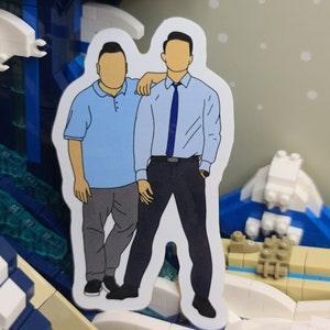 May include: A sticker featuring two figures in casual attire. One figure wears a light blue polo shirt and gray pants, while the other is in a light blue button-down shirt, dark pants, and a blue tie. The sticker has a white border.