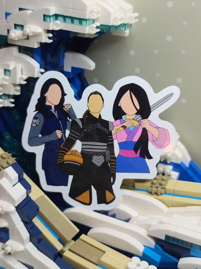 May include: A sticker featuring three stylized female figures. One wears a blue jacket with a shield emblem, another a black and gray outfit with an orange helmet, and the third a pink and blue kimono holding a sword. The sticker is set against a wave-like background.