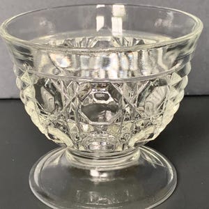 May include: Clear glass footed bowl with a diamond pattern around the sides. The bowl has a rounded top and a circular base. The glass is transparent, allowing light to pass through.