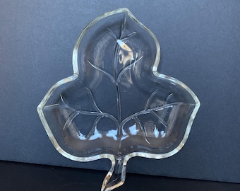 May include: A clear glass leaf-shaped serving dish with a raised design. The dish is perfect for serving snacks or appetizers.