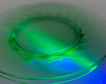 May include: A green glass plate with a wavy edge. The plate is translucent and has a slight iridescent sheen.