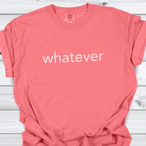 May include: Coral-coloured t-shirt with the word "whatever" printed in white across the front. The shirt has a crew neck and short sleeves. The fabric appears soft and comfortable.