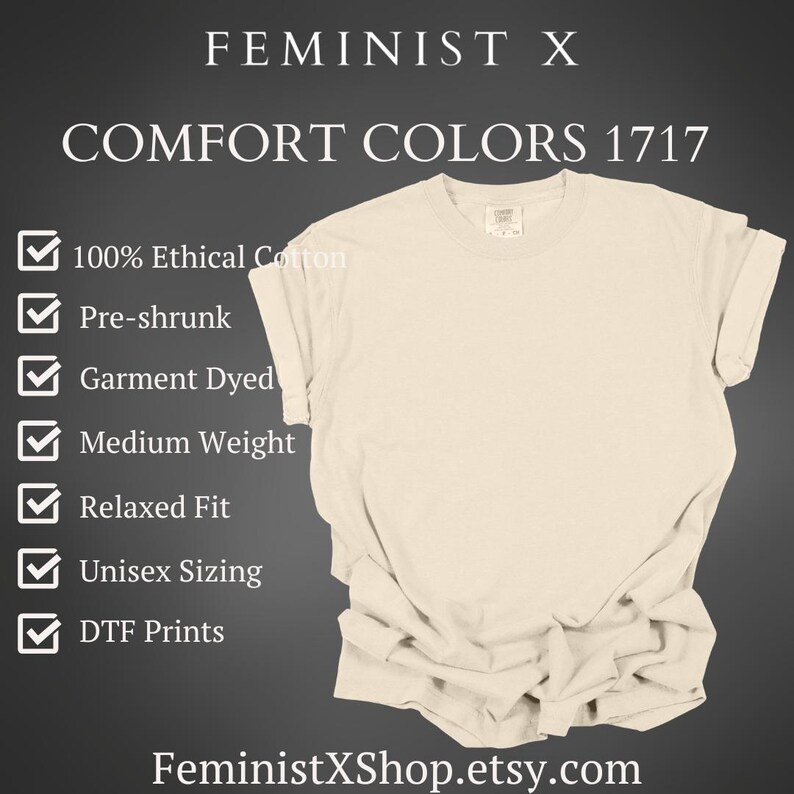 May include: Cream-colored t-shirt with rolled sleeves. The shirt features the text "FEMINIST X" and "COMFORT COLORS 1717". Additional text includes "100% Ethical Cotton", "Pre-shrunk", "Garment Dyed", "Medium Weight", "Relaxed Fit", "Unisex Sizing", and "DTF Prints".