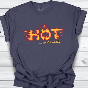 May include: Navy blue t-shirt with the word "HOT" in a fiery font, with flames in red and yellow. Below the word "HOT" is the phrase "... and sweaty" in a smaller font. The shirt is made of a soft material.