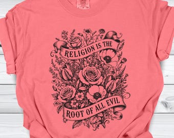May include: Coral-colored t-shirt featuring a black floral design with roses, poppies, and tulips. A banner across the center reads "RELIGION IS THE" above "ROOT OF ALL EVIL". The shirt has short sleeves and a crew neck.