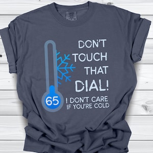 May include: Dark gray t-shirt with the text "DON'T TOUCH THAT DIAL!" and a thermometer graphic showing 65 degrees. The shirt also includes the phrase "I DON'T CARE IF YOU'RE COLD".