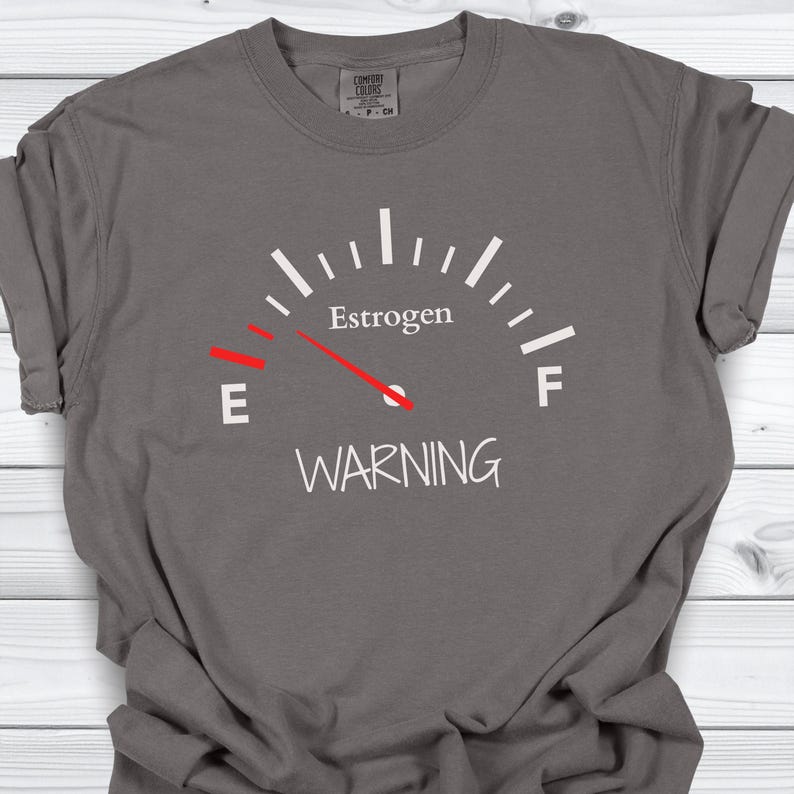May include: Gray t-shirt with a white graphic of a gauge reading "Estrogen" with a red needle pointing towards "E" and the word "WARNING" below.
