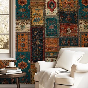 Op de afbeelding: Een gezellige woonkamer met een witte fauteuil en een crèmekleurige deken. De muren zijn versierd met behang met een patchwork-ontwerp van tapijten in teal, oranje en rood. Een kleine, ronde tafel heeft boeken en een koffiekopje.