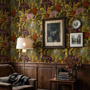 May include: A room interior featuring dark wood wainscoting and floral wallpaper in shades of mustard yellow, red, and purple. A brown armchair with a plaid throw, a floor lamp, and a side table with stacked books and a framed picture are present.