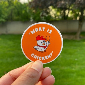 May include: A round orange sticker with a white border. The sticker features a cartoon chicken holding a drumstick and the text "What is chicken?"