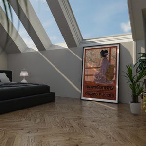 May include: A black bed frame with a black and white striped comforter and a white pillow. A white lamp sits on a nightstand next to the bed. A framed poster with the text "MADAMA BUTTERFLY" and "GIACOMO PUCCINI" hangs on the wall. A potted plant sits on the floor next to the poster.