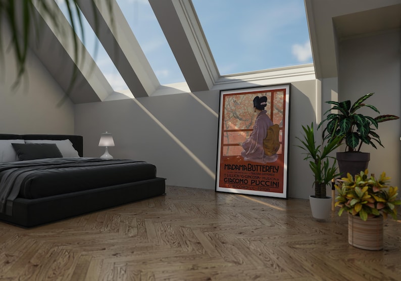 May include: A black bed frame with a black and white striped comforter and a white pillow. A white lamp sits on a nightstand next to the bed. A framed poster with the text "MADAMA BUTTERFLY" and "GIACOMO PUCCINI" hangs on the wall. A potted plant sits on the floor next to the poster.