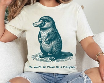 May include: A white t-shirt with a blue illustration of a platypus. The text "Be Weird. Be Proud. Be a Platypus." is printed below the illustration.