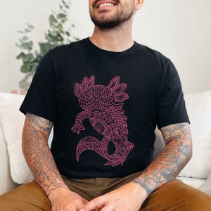 May include: A black t-shirt featuring a pink line drawing of an axolotl. The axolotl is a type of salamander with feathery gills. The design is intricate and detailed.