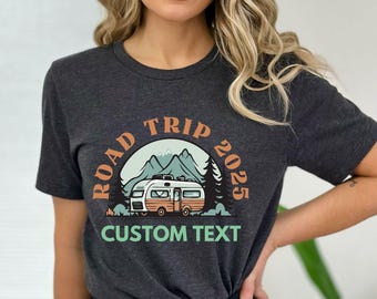 Op de afbeelding: Een donkergrijs T-shirt met een vintage-stijl grafische afbeelding van een camper voor bergen. De afbeelding bevat de tekst "Road Trip 2025" en "Custom Text".