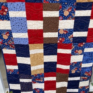 May include: A patchwork quilt with a blue, red, white, and brown color scheme. The quilt is made of various fabrics with different patterns, including stars, stripes, and a train pattern.