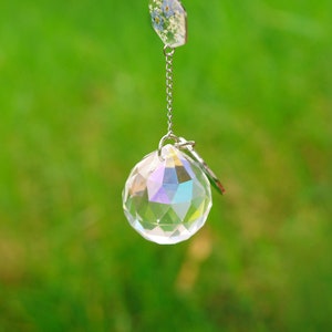 May include: A faceted clear crystal sphere with an iridescent finish suspended by a silver-toned metal chain. Attached to the top of the chain is a small hexagonal charm containing pressed blue flowers and white foliage encased in clear resin.