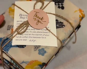 May include: A stack of four beeswax food wraps with colorful patterns, tied with twine and a pink thank you tag. The wraps are made of fabric and are reusable.