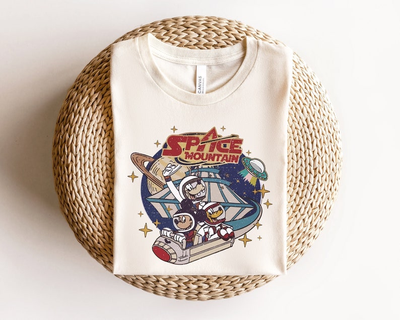 May include: A white t-shirt with a vintage-style graphic of Mickey Mouse and friends riding Space Mountain. The graphic features the words "Space Mountain" in red and white.