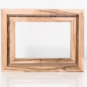 May include: A natural wood picture frame with a double border. The frame is made of light brown wood with darker brown streaks.