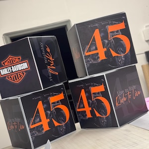 May include: Four black cardboard boxes with orange numbers and motorcycle graphics. The boxes are stacked on top of each other. The top box has the number 45 and the text "Live to Ride, Ride to Live". The second box has the number 45. The third box has the number 45. The bottom box has the Harley-Davidson logo and the text "Happy Birthday Mike".