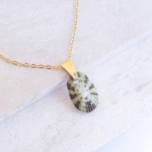 Op de afbeelding: Een goudkleurige ketting met een hanger. De hanger is een ovaalvormige steen met een patroon van groene en zwarte strepen. De ketting wordt gepresenteerd op een wit oppervlak.