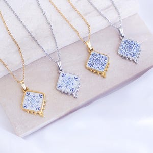 May include: Four necklaces featuring diamond-shaped pendants with blue and white floral patterns. Two necklaces have gold-toned chains and settings, while two have silver-toned chains and settings. Each pendant has small decorative metal beads at the base.
