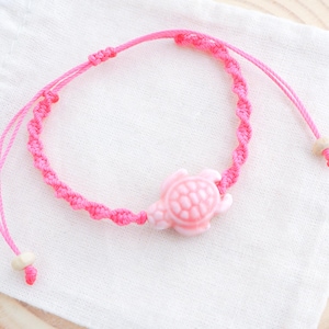 May include: Pink braided string bracelet with a pink turtle charm.