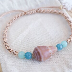 May include: A light brown braided cord bracelet with a light brown seashell charm and three light blue and green glass beads.