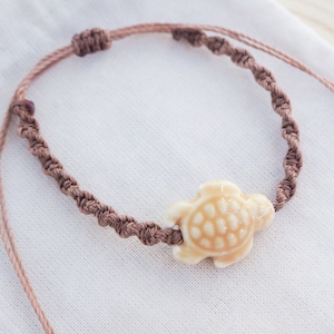 Op de afbeelding: Een bruin gevlochten koord armband met een beige keramische schildpad bedel.