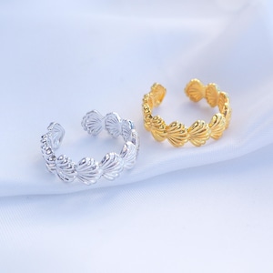 Op de afbeelding: Twee verstelbare schelpenringen, één zilver en één goud, worden getoond op witte stof. De ringen hebben een gedetailleerd schelpenontwerp, ideaal om een vleugje kustcharme toe te voegen. Het open ontwerp maakt maatverstelling mogelijk.