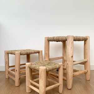 Könnte beinhalten: Drei Holzhocker mit geflochtenen Strohsitzen. Die Hocker sind unterschiedlich groß, der größte hinten und der kleinste vorne. Die Hocker sind aus Naturholz gefertigt und haben einen rustikalen Look.