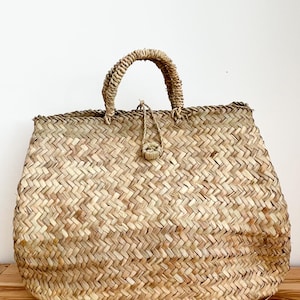 Könnte beinhalten: Eine große, naturgeflochtene Strohtasche mit einem einzigen Henkel. Die Tasche ist aus einem hellbraunen, natürlichen Material gefertigt und hat ein geflochtenes Muster.