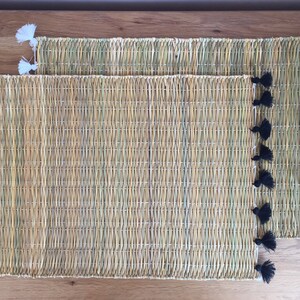 Peut inclure: Deux sets de table tissés avec des pompons noirs et blancs. Les sets de table sont faits de matériaux naturels et ont une couleur brun clair.