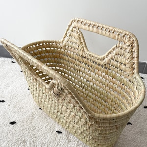 May include: A woven straw basket with two handles. The basket is light brown and has a rectangular shape.