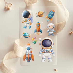 Könnte beinhalten: Ein Set mit neun Stickern zum Thema Weltraum mit Astronauten, Raketen, Planeten und Sternen. Die Sticker sind bunt und fantasievoll und perfekt, um jedem Projekt eine lustige Note zu verleihen.