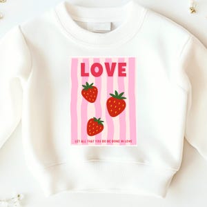 Bügelbild Love mit Erdbeeren aufgebügelt auf einem weißen Kinder Sweatshirt als Anwendungsbeispiel