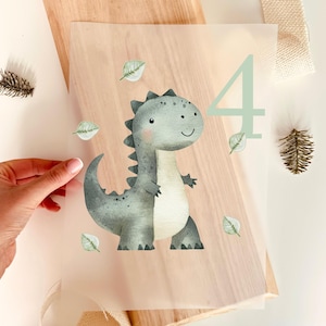 Op de afbeelding: Een aquarel illustratie van een vriendelijke, grijze dinosaurus met een groen nummer 4. De dinosaurus heeft een vrolijke uitdrukking en is omringd door kleine groene blaadjes. De afbeelding staat op een doorschijnend vel.