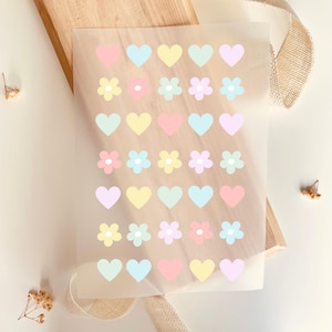 Könnte beinhalten: Eine Blatt mit Aufklebern in Pastellfarben in Form von Herzen und Blumen. Die Herzen sind in den Farben Rosa, Gelb, Blau und Grün. Die Blumen sind in den Farben Gelb, Rosa und Blau.
