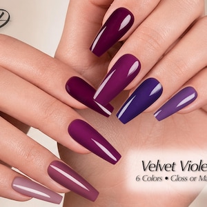 May include: Long coffin-shaped nails featuring a gradient of purple shades ranging from deep plum to light mauve. The nails have a smooth, reflective finish. Text on the image reads: Velvet Violet, 6 Colors • Gloss or Matte, with a stylized D logo.