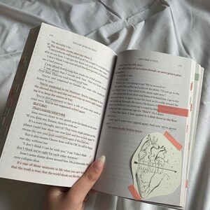 Pode incluir: Um close-up de um livro com uma ilustra&ccedil;&atilde;o de cora&ccedil;&atilde;o rosa e branco na p&aacute;gina. O livro est&aacute; aberto em uma p&aacute;gina com o texto "One True Loves" e "The same hearts, broken twice."