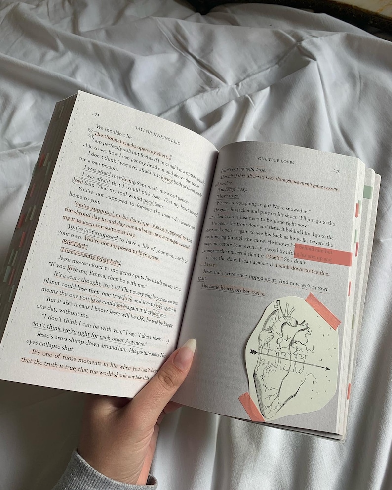 Pode incluir: Um close-up de um livro com uma ilustra&ccedil;&atilde;o de cora&ccedil;&atilde;o rosa e branco na p&aacute;gina. O livro est&aacute; aberto em uma p&aacute;gina com o texto "One True Loves" e "The same hearts, broken twice."