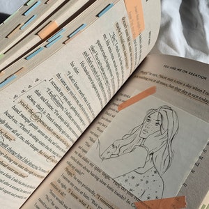 Pode incluir: Um close-up de um livro com uma ilustra&ccedil;&atilde;o desenhada &agrave; m&atilde;o de uma mulher com cabelo comprido. O livro est&aacute; aberto em uma p&aacute;gina com texto sobre f&eacute;rias. O texto inclui a frase "You and Me on Vacation".