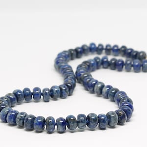 May include: A long necklace made of dark blue lapis lazuli beads. The beads are round and have a slightly irregular shape. The necklace is strung on a thin cord.